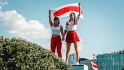 Two women display a former Belarusian national flag, a symbol of opposition to the government,  during a Minsk rally on August 16, 2020 against police violence and Belarus' official presidential election results.