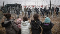 Migrant children stand in front of a barbed wire fence and Polish servicemen on the Belarusian side of Poland's Kuznitsa checkpoint  on November 17, 2021, as reports first surfaced of the migrants' withdrawal from the area, under Belarusian forces' supervision. 